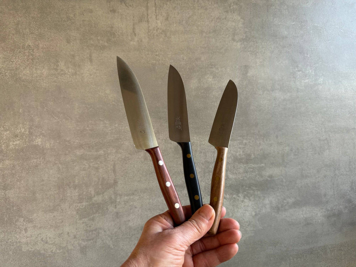 Eine Hand hält 3 Windmühlenmesser K3 mit 3 verschiedenen Holzgriffen in der Hand.