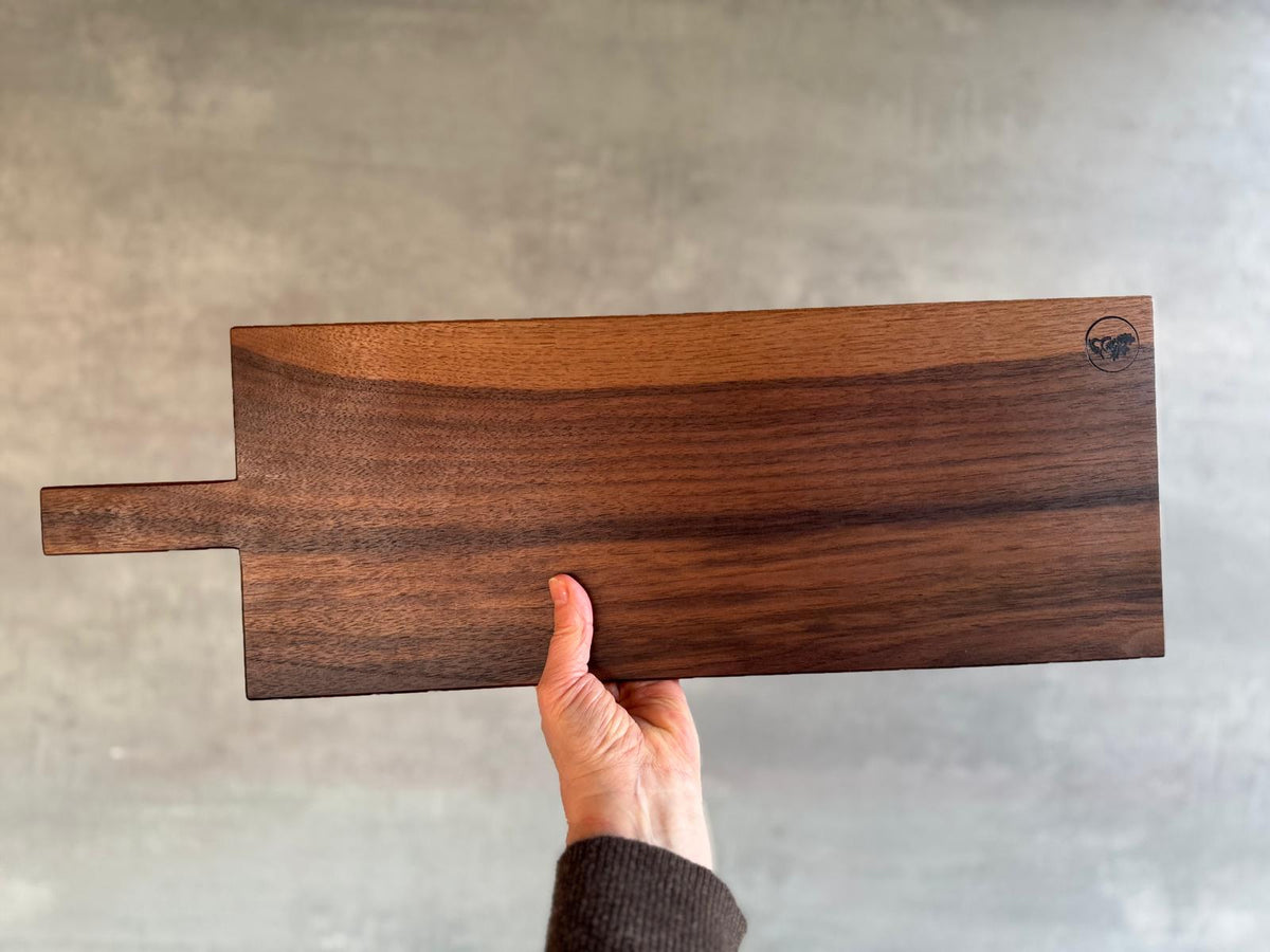 In der Hand ein 60 cm langes Servierbrett aus einem Stück Nussbaum