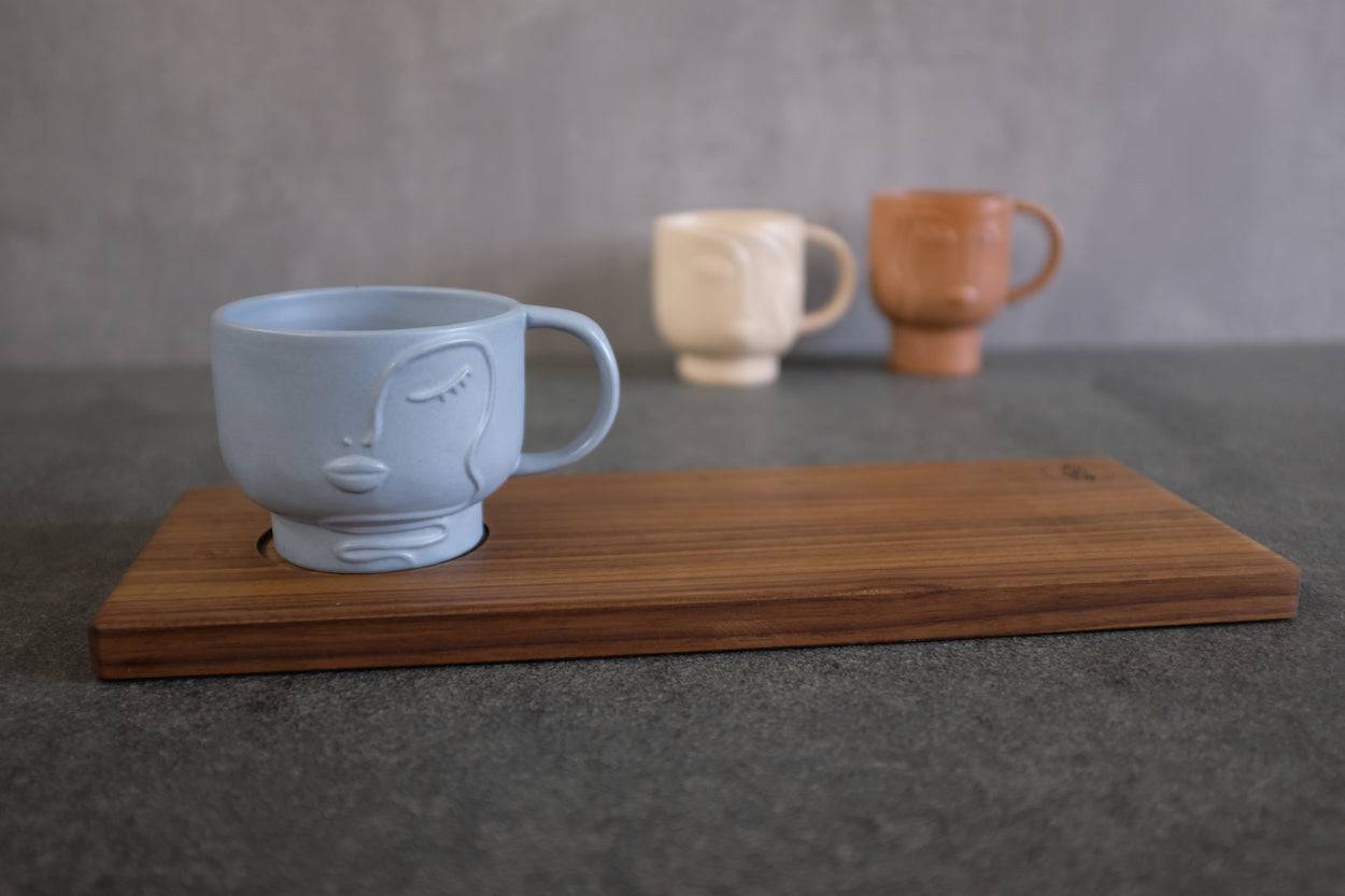 Rechteckiges Holz Tablett aus Nussbaum massiv mit einer Vertiefung für einen Becher. Dekoriert mit einer blauen Keramik Tasse mit Gesicht.