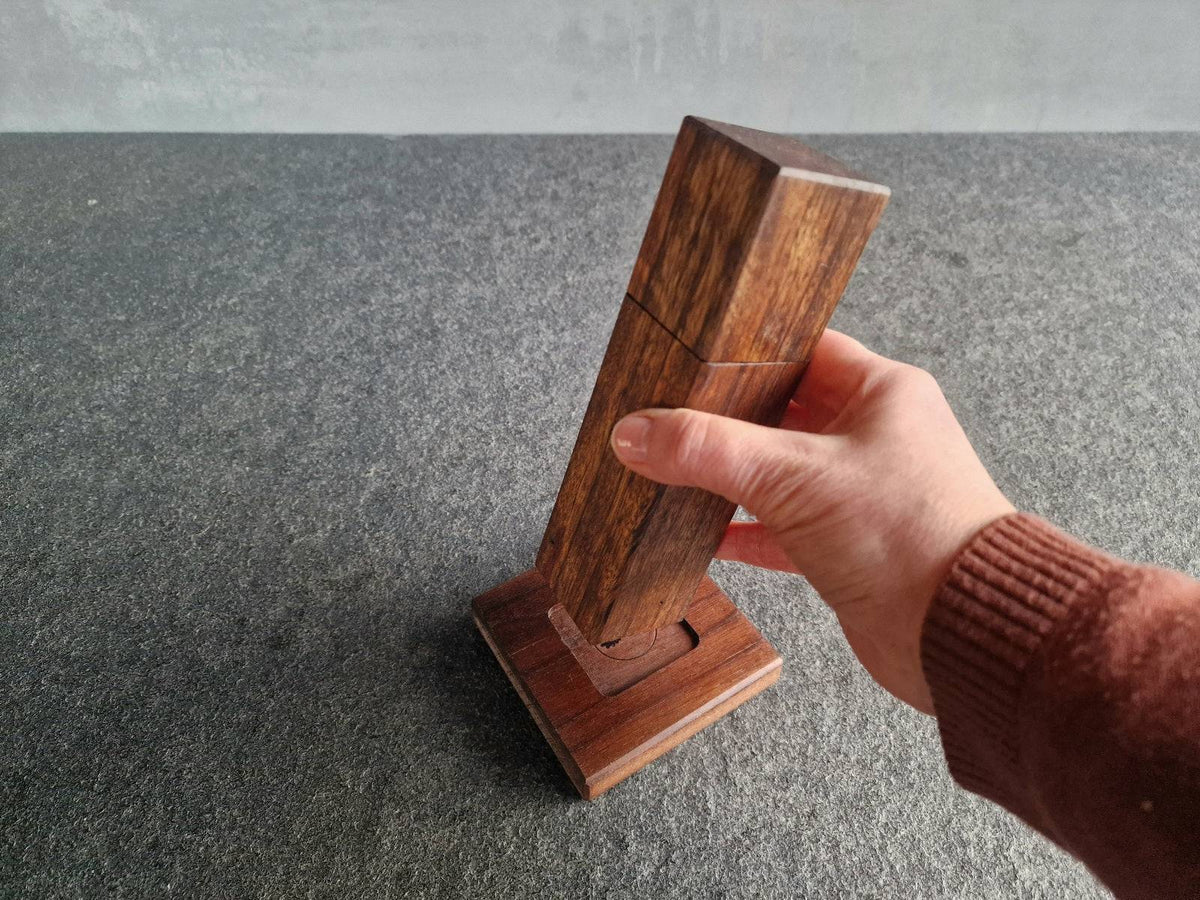 Hand hält eine Pfeffermühle aus Ovenkol  über einem Untersetzer aus Nussbaum.