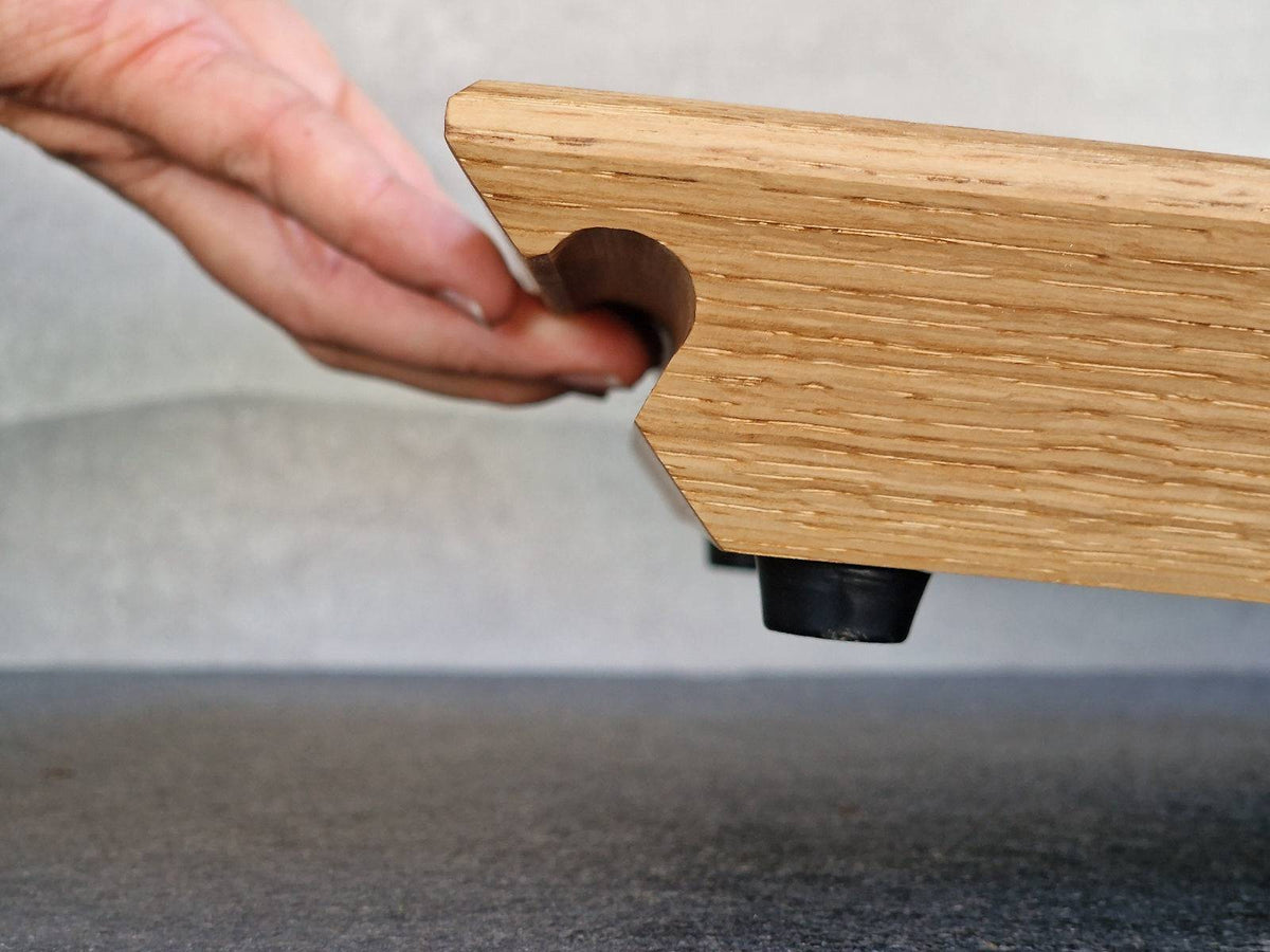 Hand hebt in der Griffmulde ein massives Premium Gleitbrett aus Eiche.
