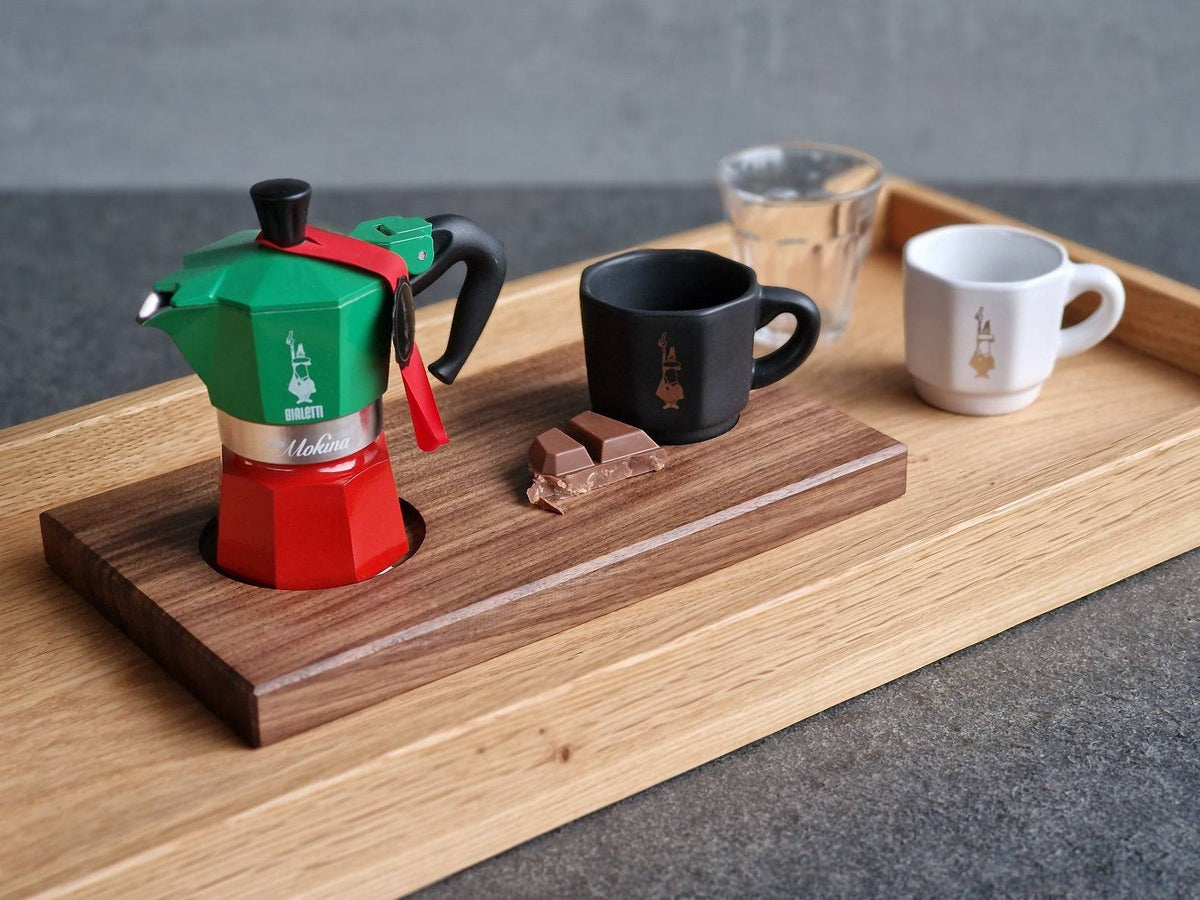 Moka Express Kocher von Bialetti mit einer weißen und einer schwarzen Bialetti Espressotasse auf einem Espressotablett aus Nussbaum. Auf einem Eiche Tablett. 