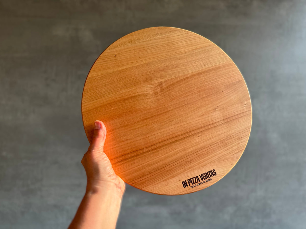 Hand hält ein rundes Kirschbaum Pizzabrett in die Höhe.