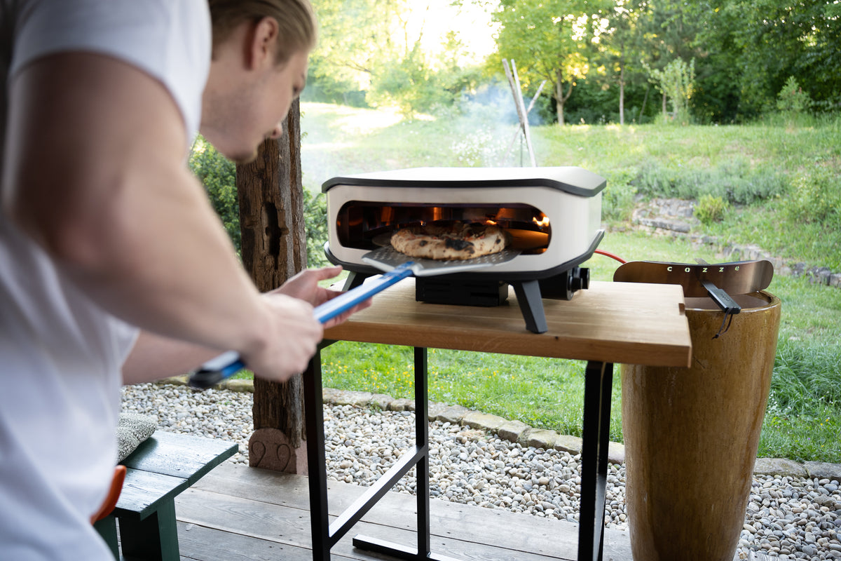 Pizzabäcker holt gerade eine Pizza aus einem Pizza Cozze Ofen mit einer Schaufel von Gi.Metall
