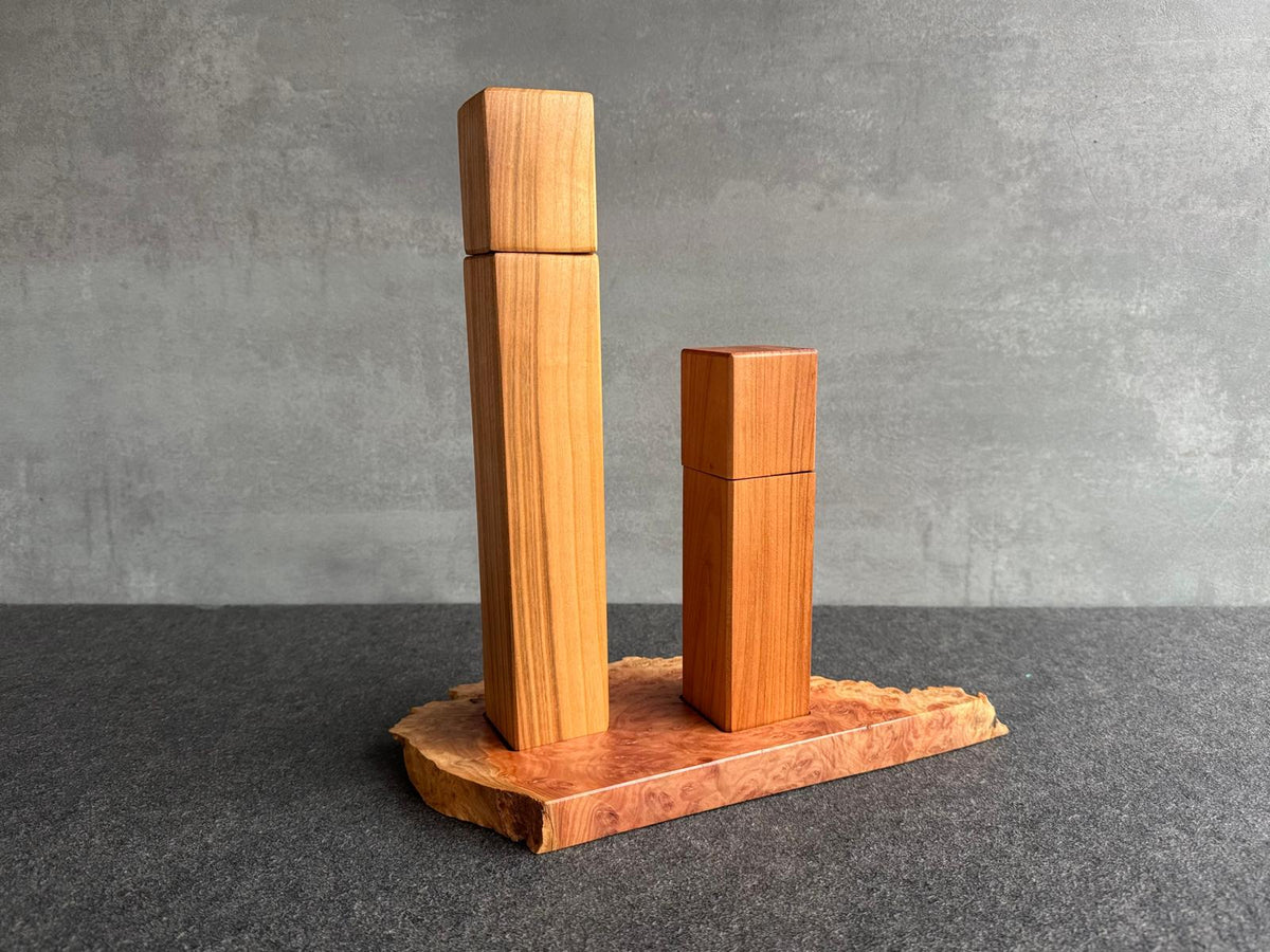 Vorne im Bild die hohe Pfeffermühle, dahinter die kleinere Salzmühle, beides aus Kirschbaum. Die Mühlen stehen auf einem Untersetzer aus Goldfield