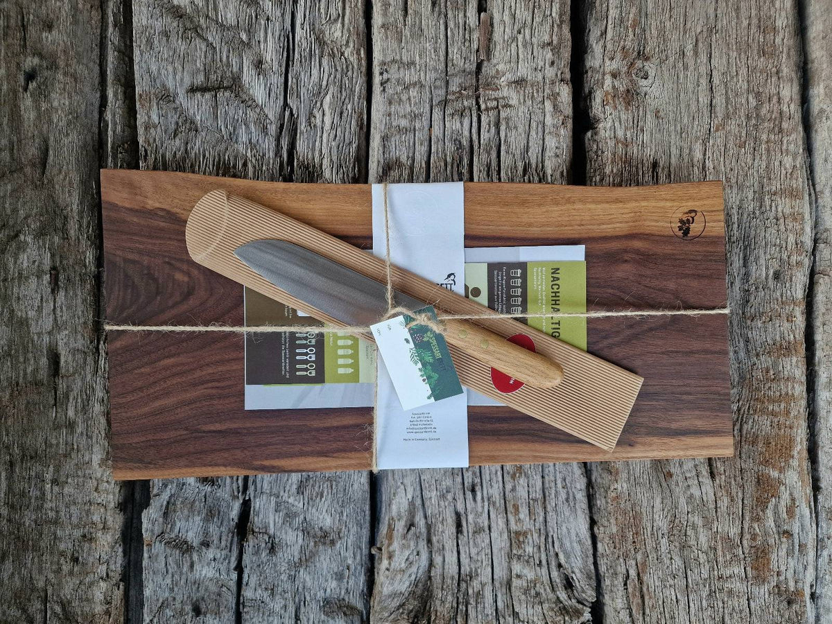 Geschenkset: Bestehend aus einem Nussbaum Vollholz Schneidebrett mit Baumkante und einem Windühlenmesser Santoku. Wellverpackung mit Paketschnur und Geschenkanhänger. Flyer, Pflegeanleitung und Schleifpapier dabei. 