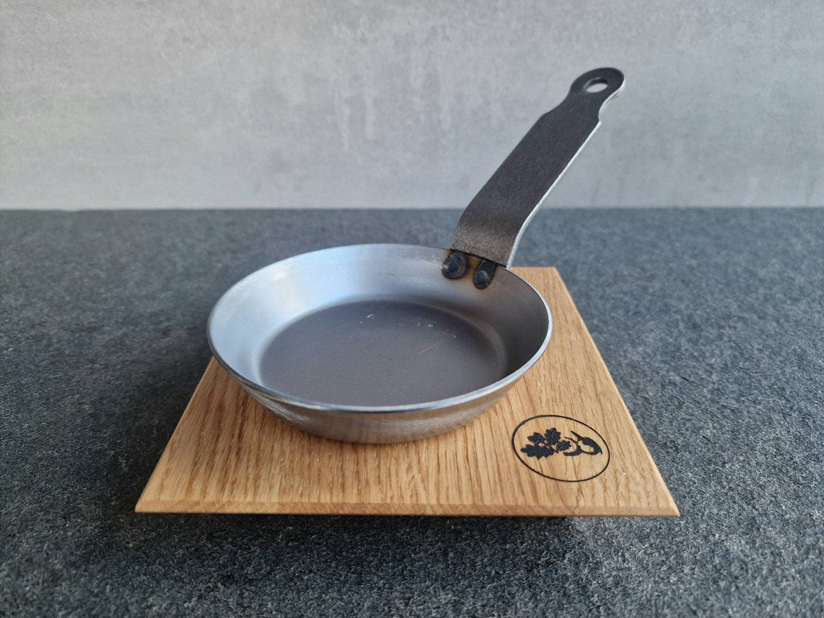 Kleine Tapas Eisenpfanne auf einem Eichenholz Topfuntersetzer von Spessartbrett.