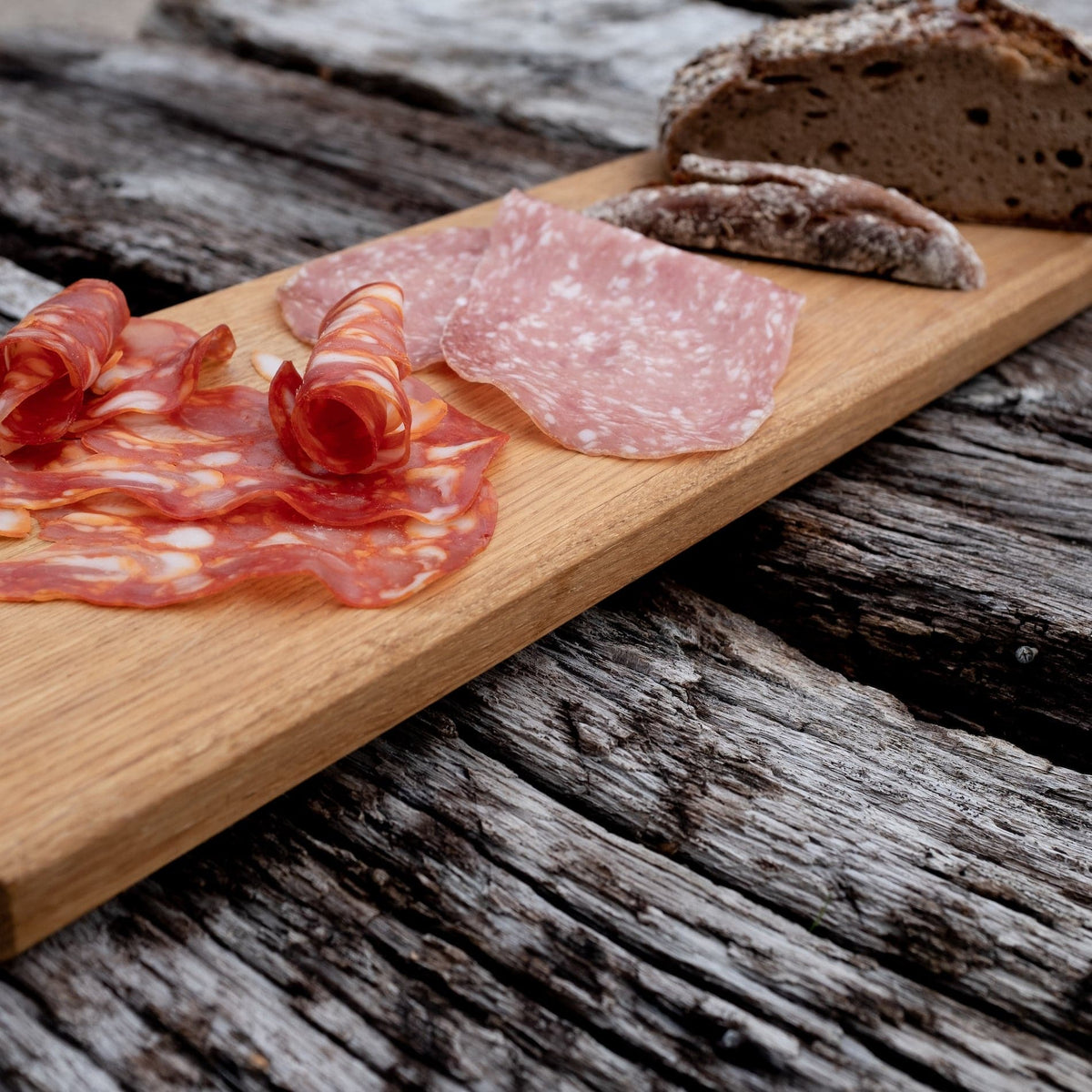 Detailaufnahme eines Eiche Brettes auf dem Wurst und ein Brot liegt.